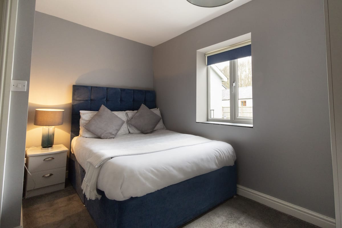 A bedroom with a bed, bedside table, lamp, and window.