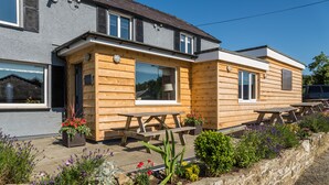 A wooden cabin-style building with a patio area, outdoor seating, and a stone retaining wall. - The Slate (Bangor)