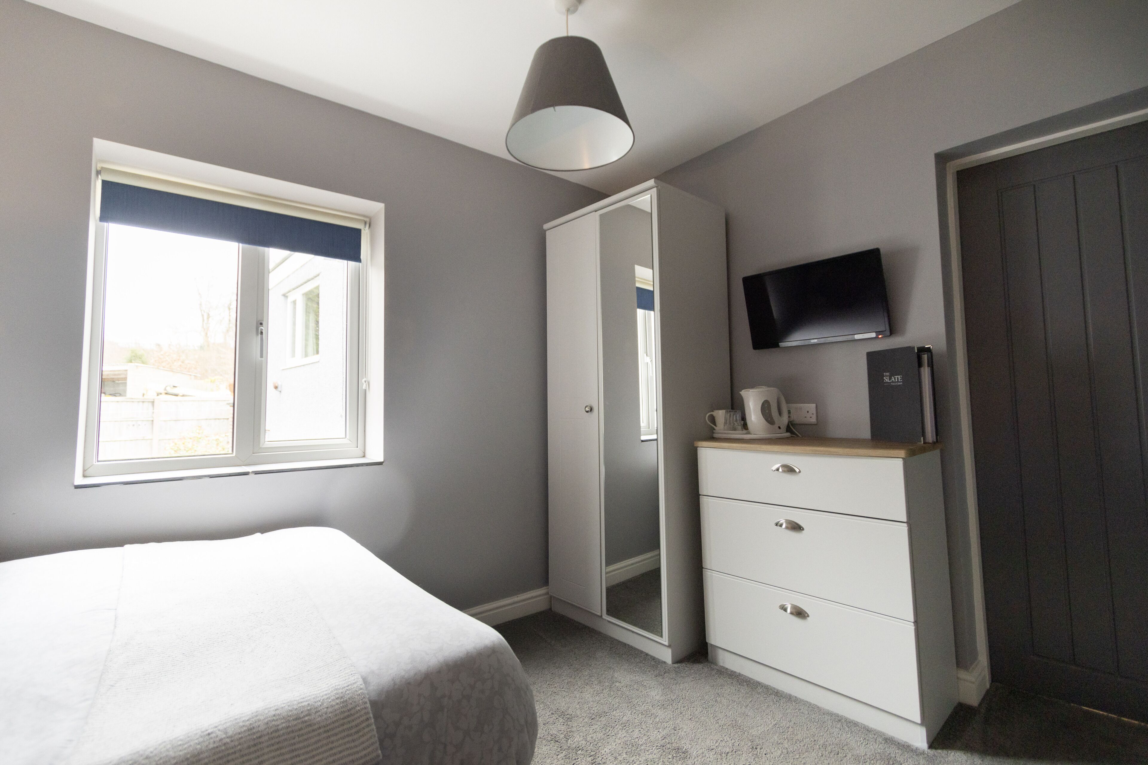 Une chambre à coucher avec un lit, une armoire, une télévision et une fenêtre.