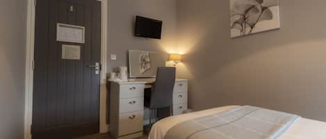 Una habitación de hotel con cama, escritorio, silla y televisor de pantalla plana montado en la pared.