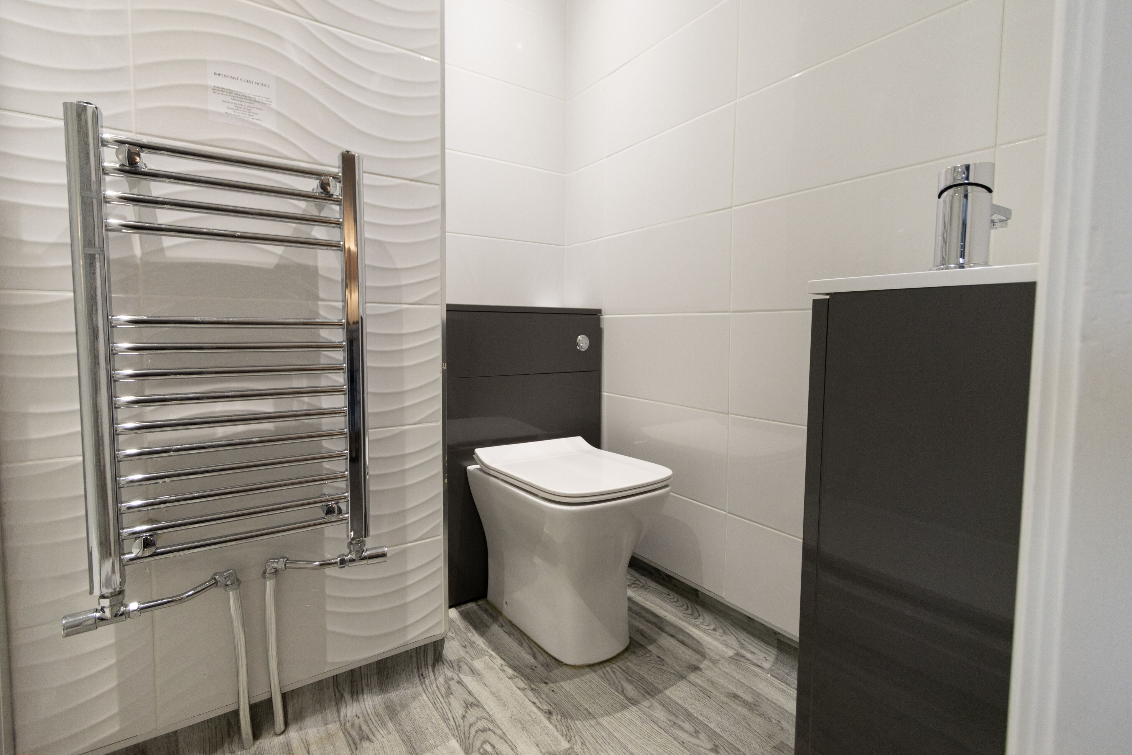 Un baño moderno con un toallero cromado, un inodoro blanco y un mueble oscuro.