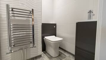 Un baño moderno con un toallero cromado, un inodoro blanco y un mueble oscuro.