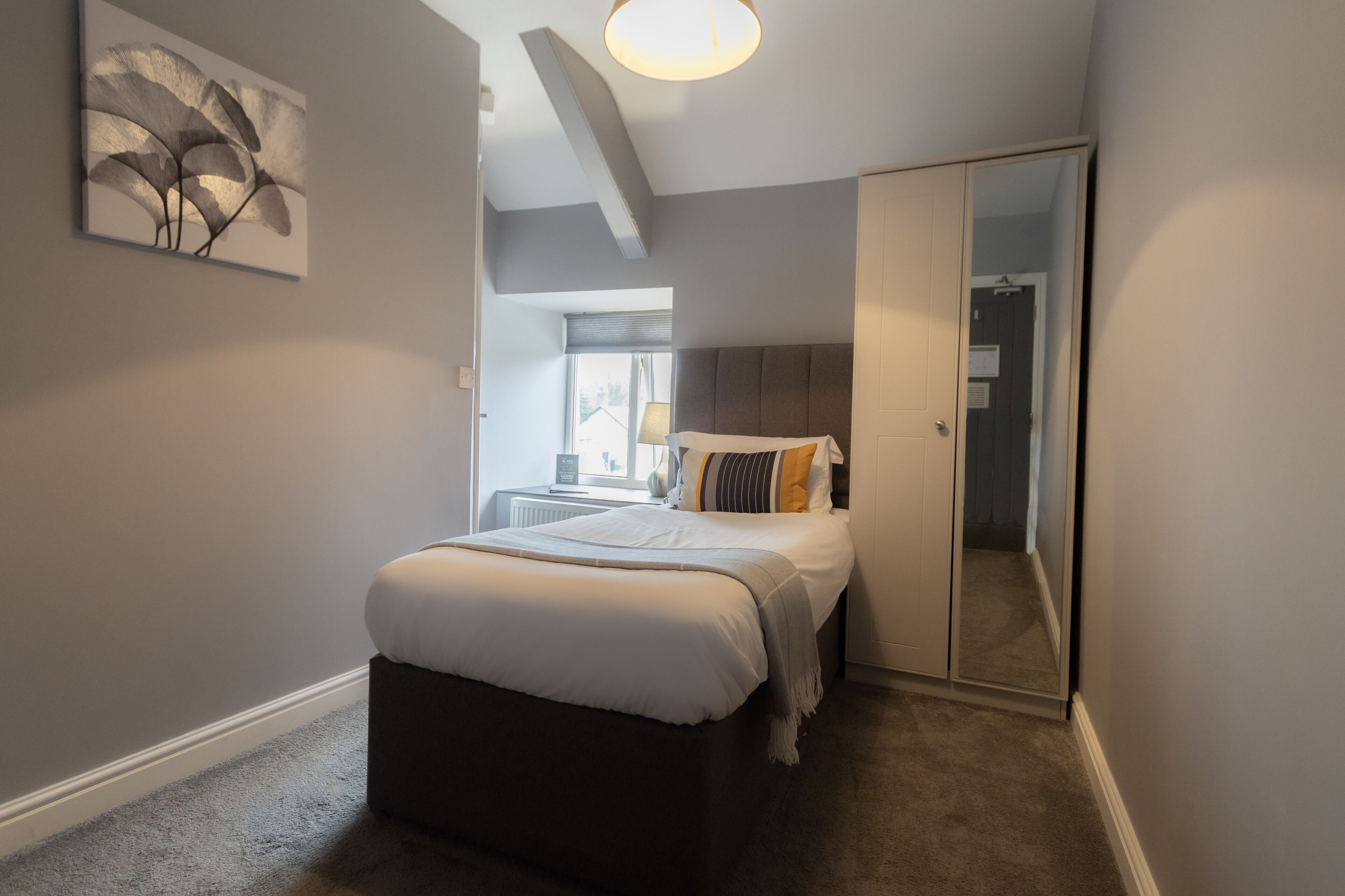 A bedroom with a bed, a bedside table, a mirror, and a window.