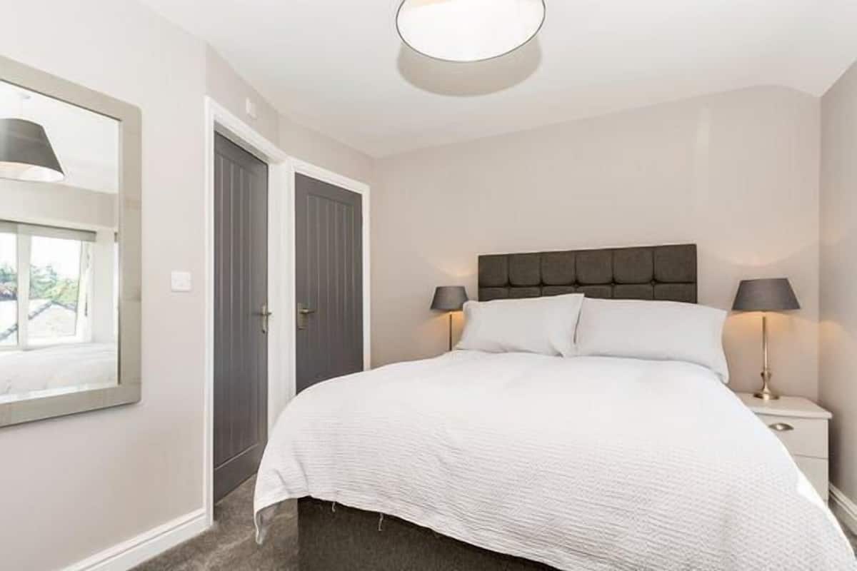 A bedroom with a bed, bedside lamps, a window, and a door.