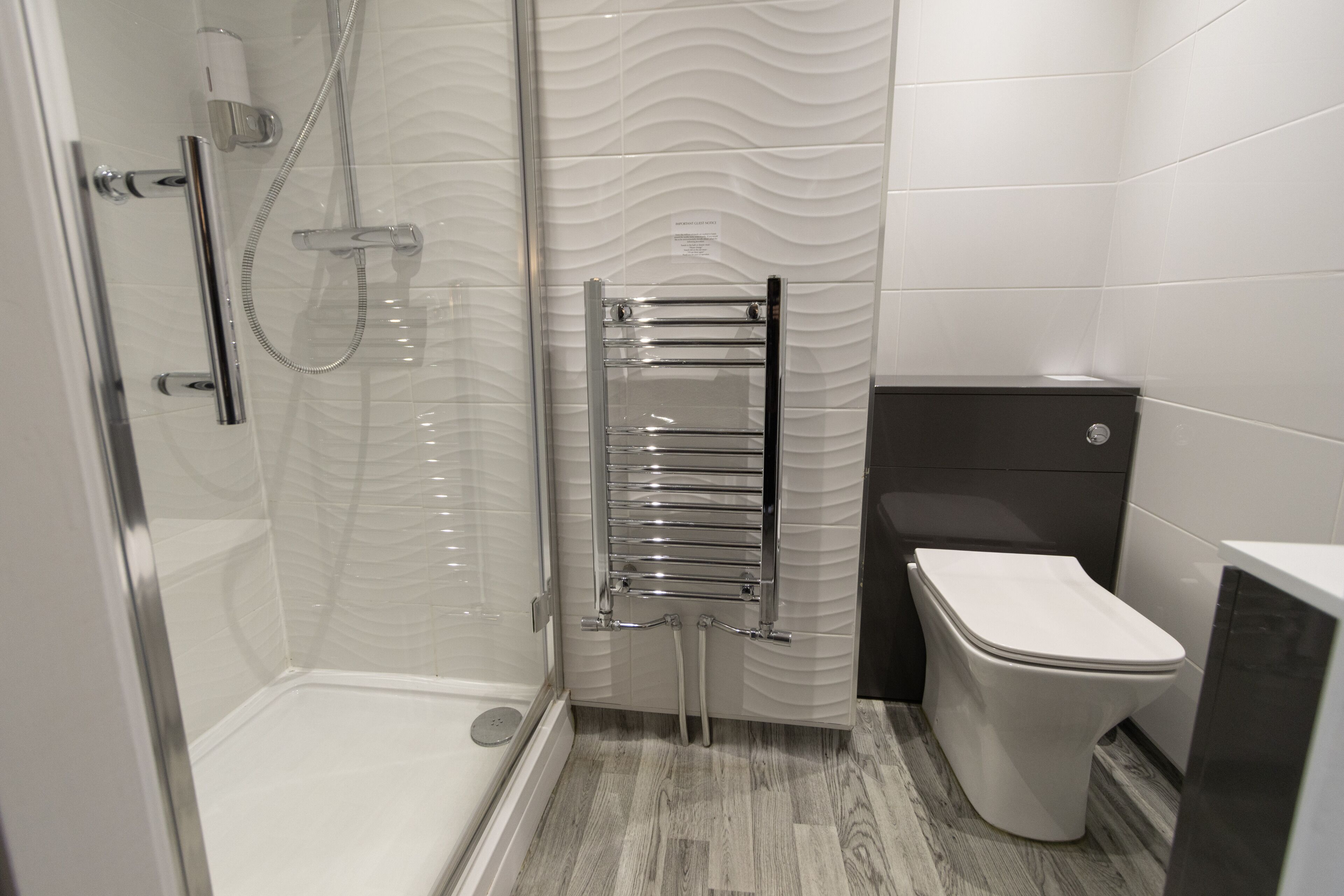 Un baño moderno con cabina de ducha de vidrio, toallero cromado, inodoro y lavamanos.