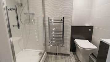 Un baño moderno con cabina de ducha de vidrio, toallero cromado, inodoro y lavamanos.
