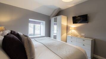 A bedroom with a large bed, a wardrobe, a desk, and a television on the wall.
