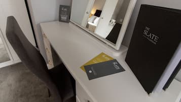 Et hotelværelse med et hvidt skrivebord, et spejl, en sort mappe mærket "The Slate" og et skilt, der angiver "The Slate uden for åbningstid".