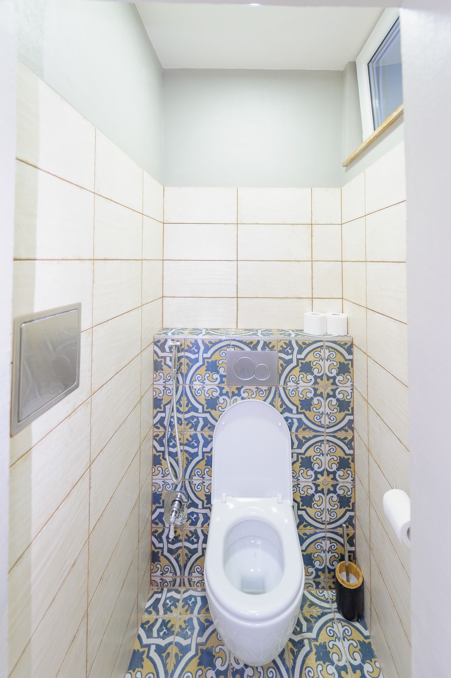 Ein kleines Badezimmer mit Toilette, gemusterten Fliesen und einem Fenster.