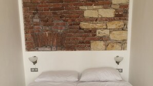 A bed with white bedding, two wall-mounted light fixtures, and a brick and stone wall above. - Pinkova Apartments (Prague)