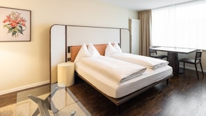 Een hotelkamer met een bed, nachtkastje, lamp, bureau, stoel en een raam met gordijnen.