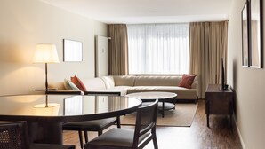 Een moderne hotelkamer met een ronde eettafel, een bank, een klein bijzettafeltje en een lamp.
