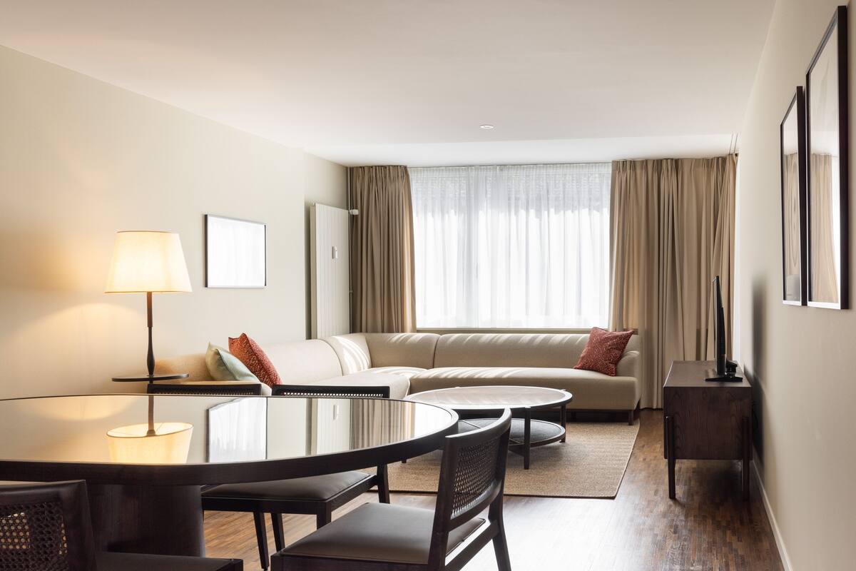 Une chambre d’hôtel moderne avec une table à manger ronde, un canapé, une petite table d’appoint et une lampe.