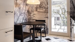 Een eetruimte met een zwart-wit schakerend vloertje, een tafel met stoelen, een hanglamp en een muurschildering van een tropisch landschap.