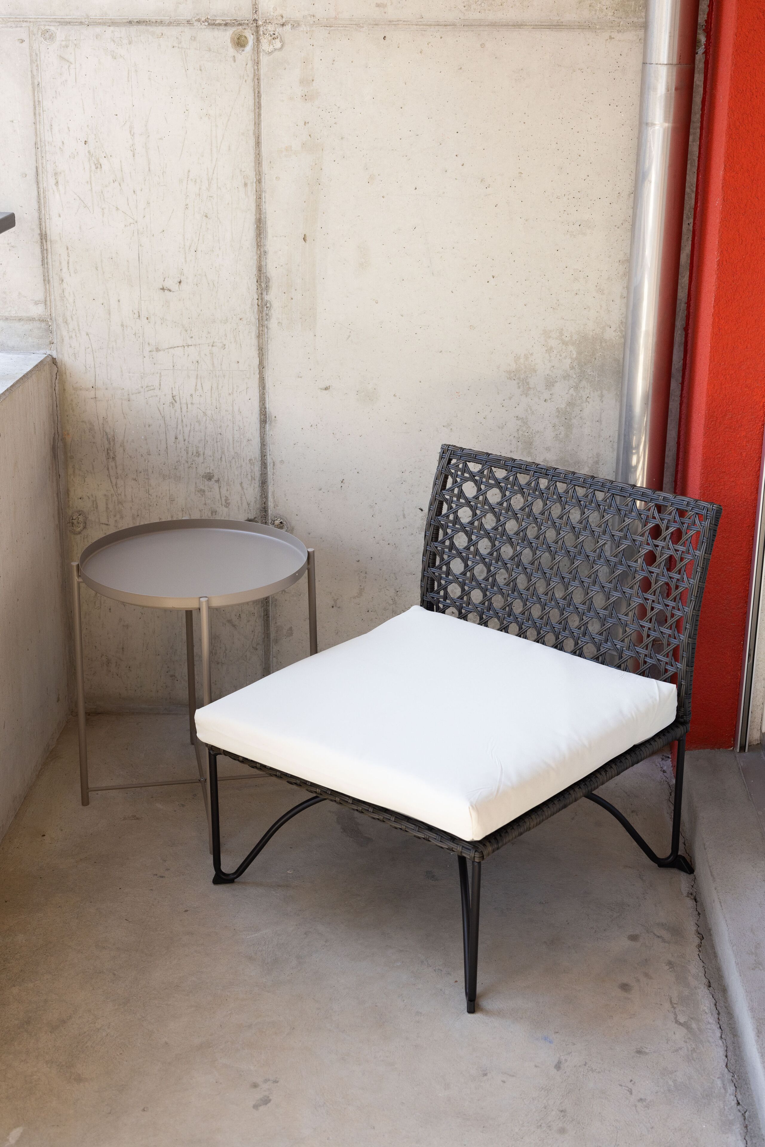 A chair with a white cushion and a metal frame, positioned next to a small round table with a metal frame.