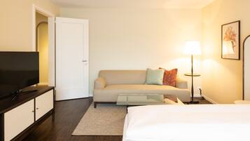 A hotel room with a bed, a sofa, a TV on a cabinet, a lamp, and a painting on the wall.