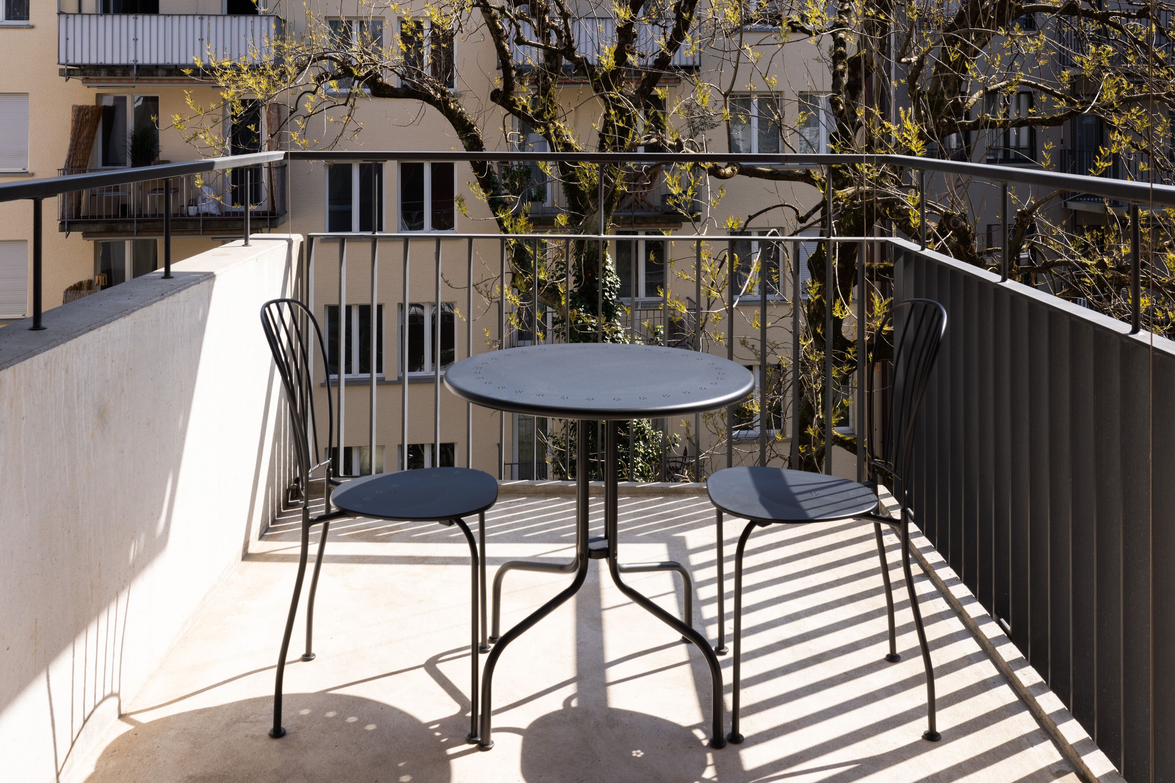 A balcony with a round table and two chairs, surrounded by a metal railing.
