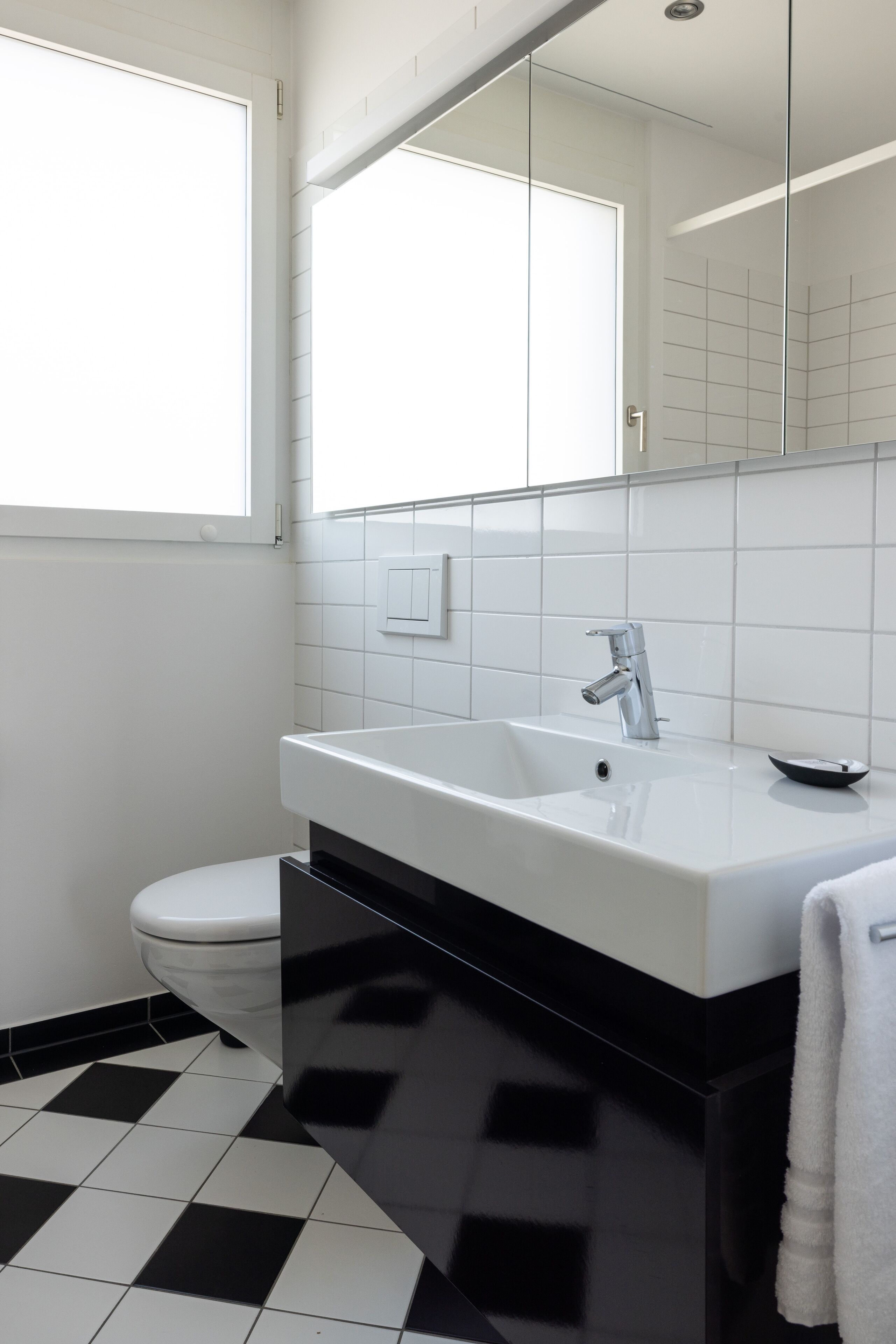 Un baño moderno con un lavabo blanco, un inodoro y un espejo grande.