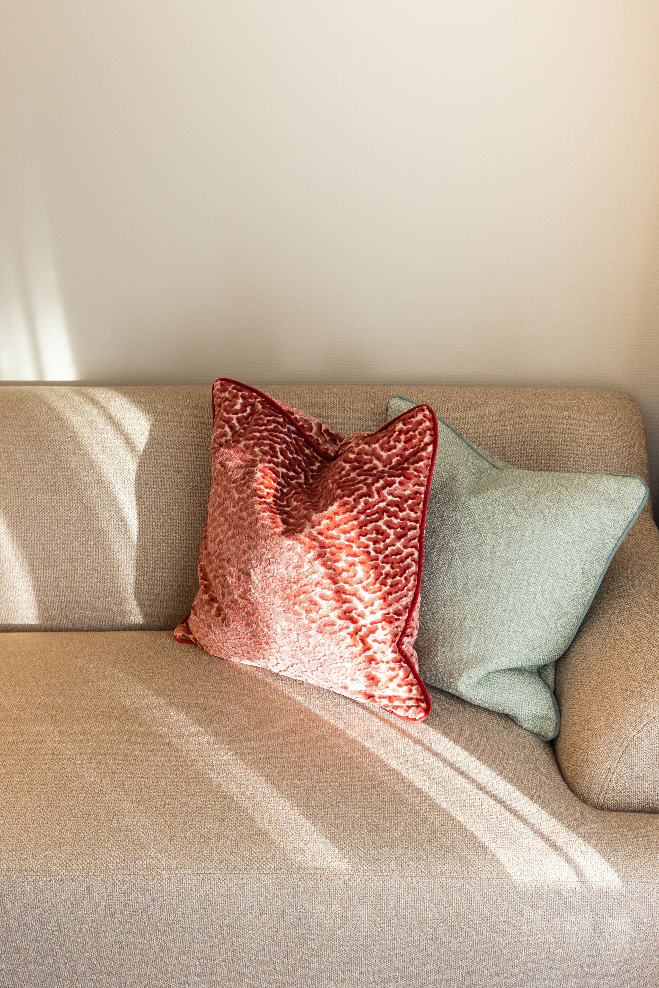 En beige soffa med två kuddar, en röd och en grön.