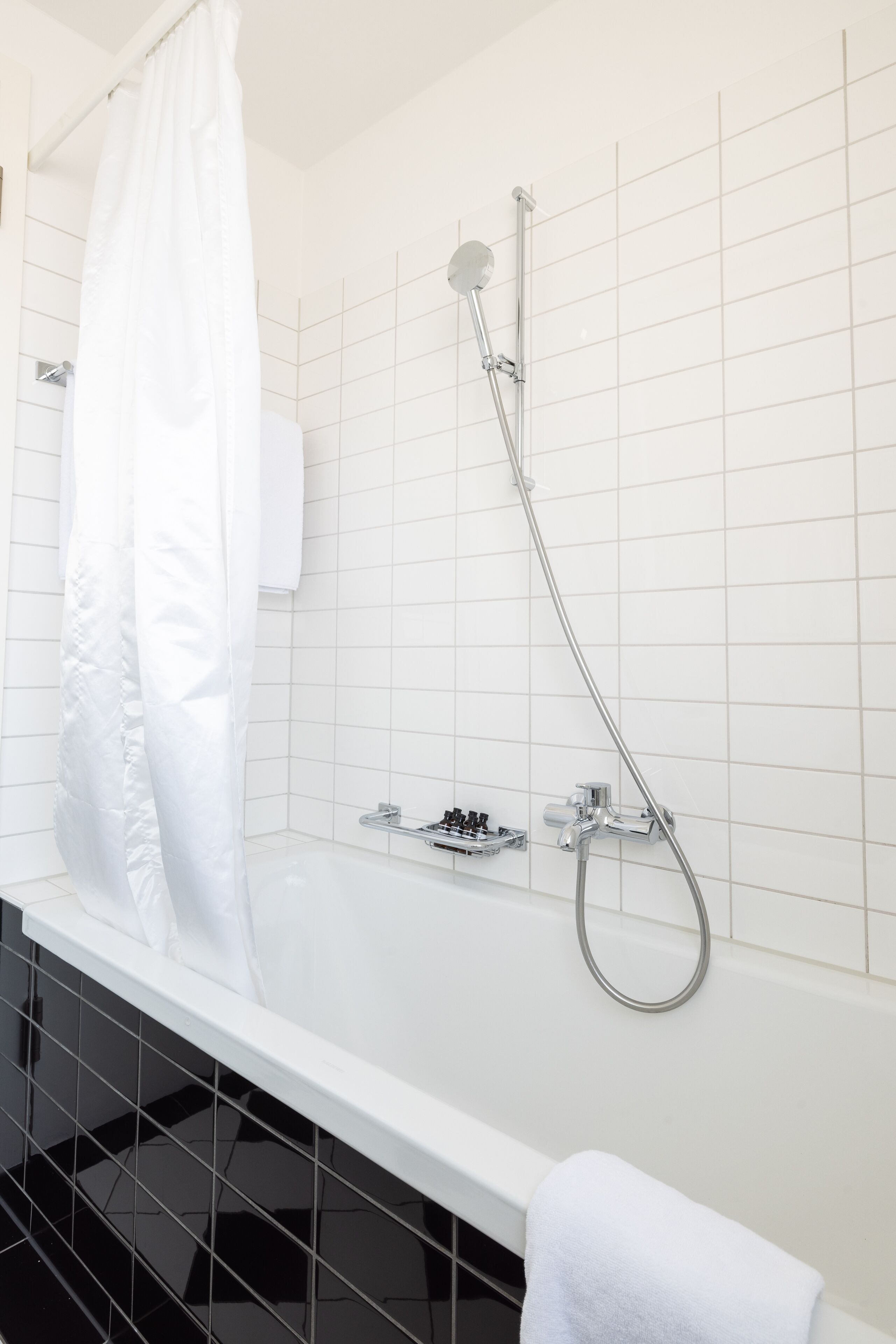A modern bathroom with a white bathtub, chrome fixtures, and a tiled wall.
