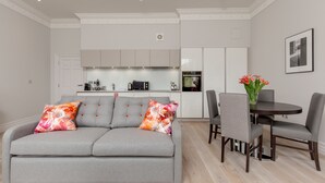 A modern living room with a grey sofa, a dining table with chairs, and a kitchen in the background. - Destiny Scotland Chisholm Hunter Suites (Edinburgh)