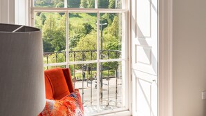 A room with a large window, a sofa with a colorful cushion, and a lamp. - Destiny Scotland Chisholm Hunter Suites (Edinburgh)