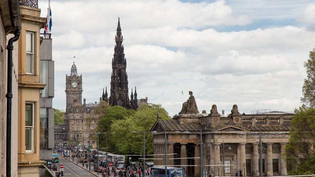A busy street with buses, pedestrians, and historic buildings including a clock tower. - Destiny Scotland Chisholm Hunter Suites (Edinburgh)