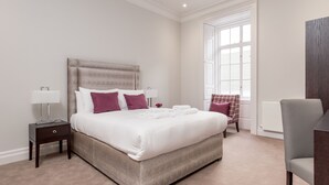 A neatly arranged bedroom with a large bed, bedside tables, a chair, and a window with blinds. - Destiny Scotland Chisholm Hunter Suites (Edinburgh)