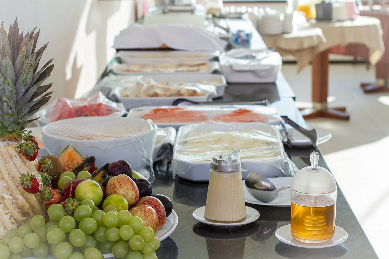 Una mesa de buffet con distintos alimentos, incluyendo frutas, quesos y un dispensador de bebidas.