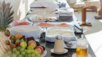 Una mesa de buffet con distintos alimentos, incluyendo frutas, quesos y un dispensador de bebidas.