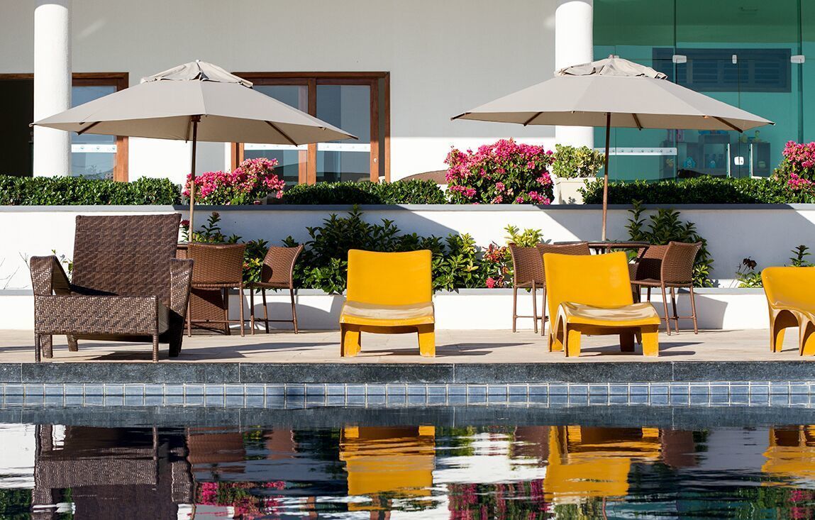 A poolside area with wicker chairs, yellow chairs, and umbrellas.