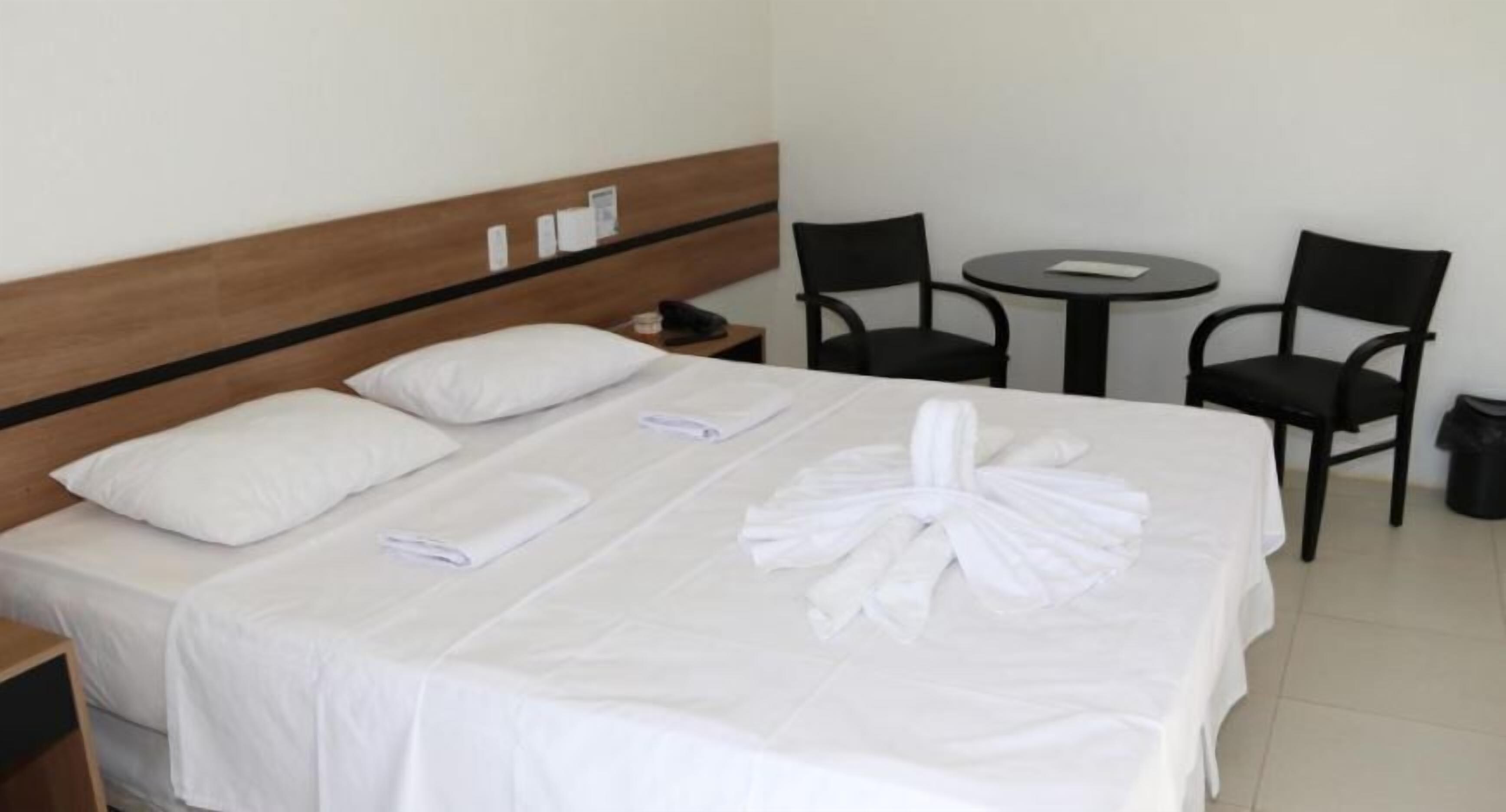 A hotel room with a neatly made bed, two chairs, a small round table, and a nightstand with a phone.
