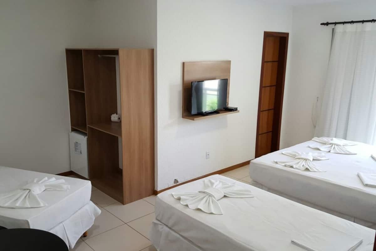Une chambre d’hôtel avec deux lits, un téléviseur fixé au mur, une armoire en bois et un petit bureau avec une chaise.
