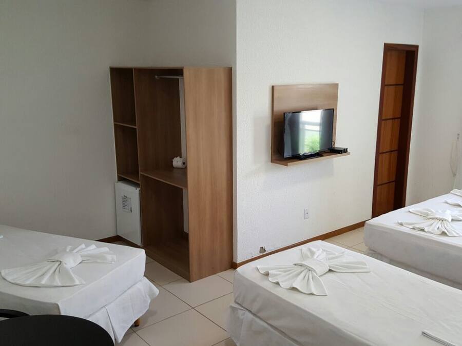 A hotel room with two beds, a TV mounted on the wall, a wooden wardrobe, and a small desk with a chair.