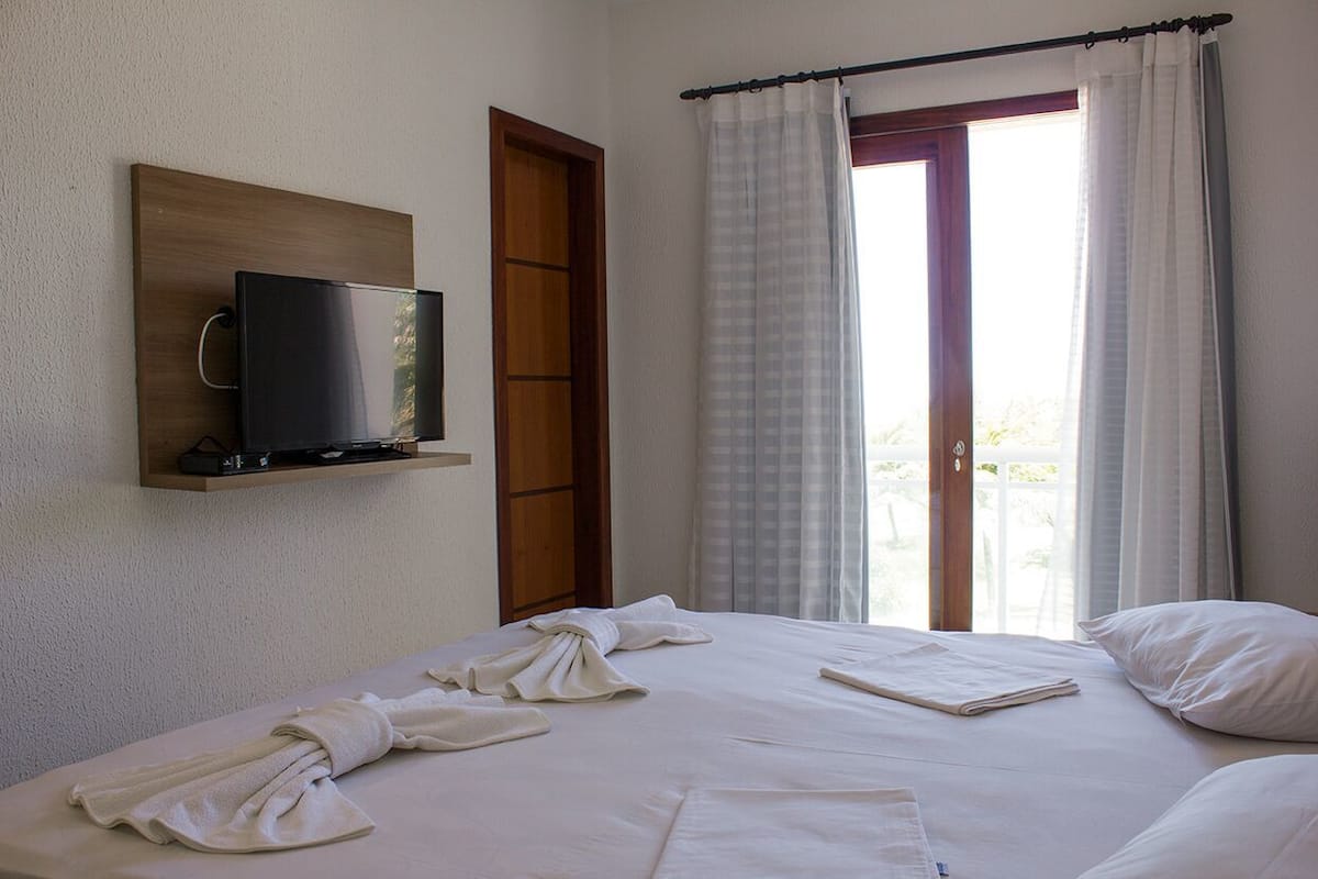 Une chambre d’hôtel avec un lit, un téléviseur fixé au mur et une vue sur l’extérieur par une fenêtre.