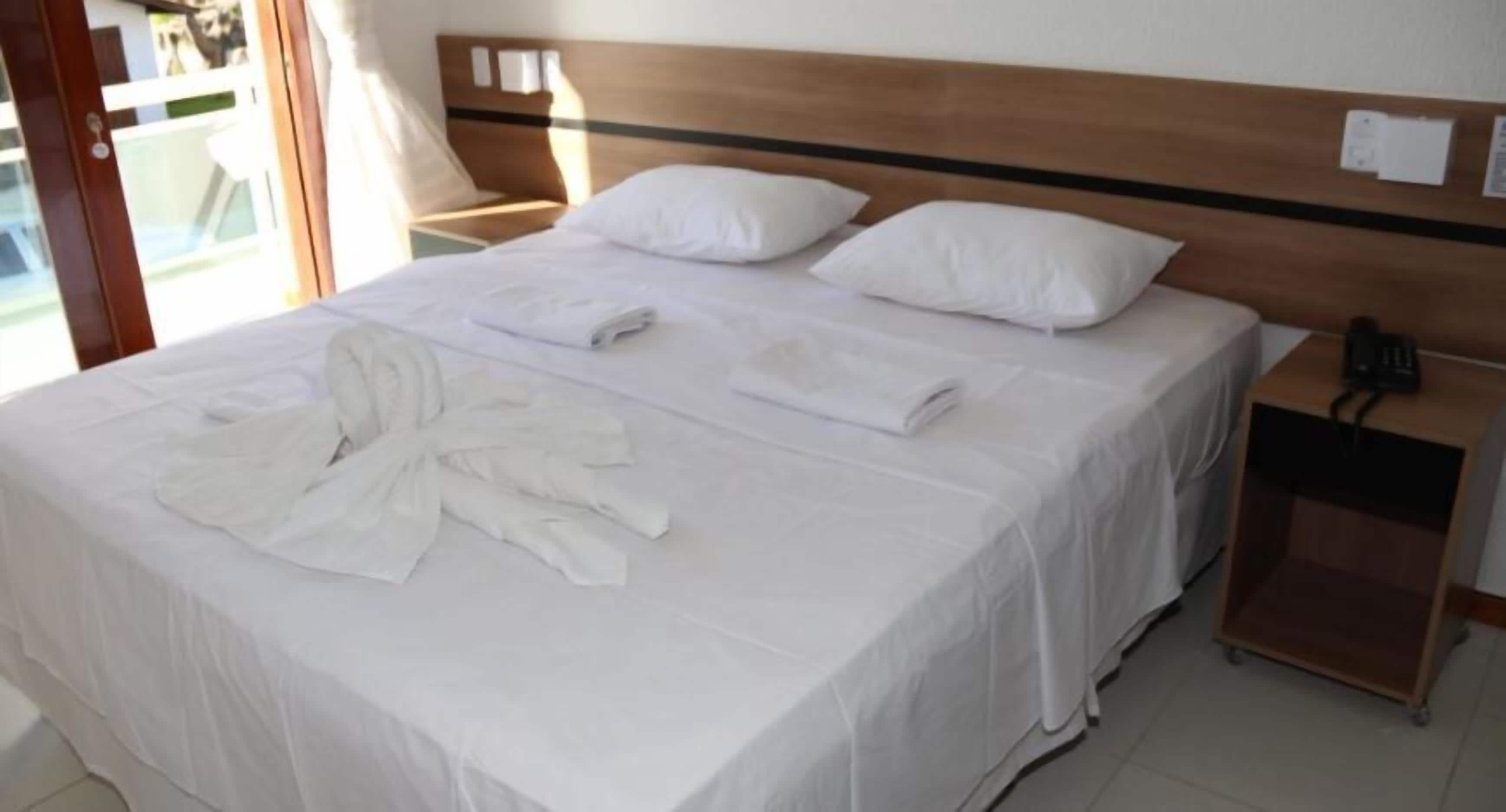 Una habitación de hotel con una cama grande, dos almohadas y ropa de cama impecable, incluyendo una bata.