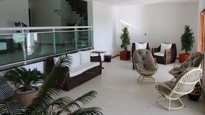 Una sala de estar moderna con barandilla de vidrio, muebles de mimbre y plantas en macetas.