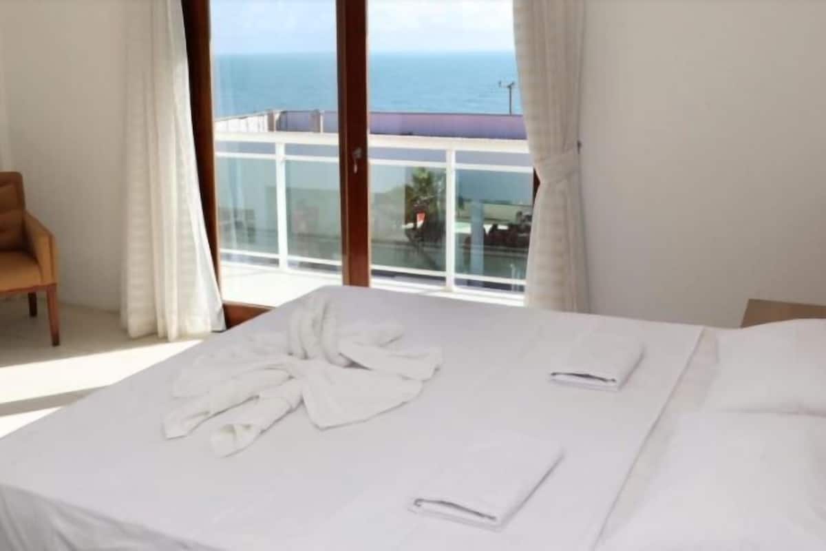 Une chambre d’hôtel avec un lit, une chaise et une vue sur la mer, grâce à de grandes fenêtres.