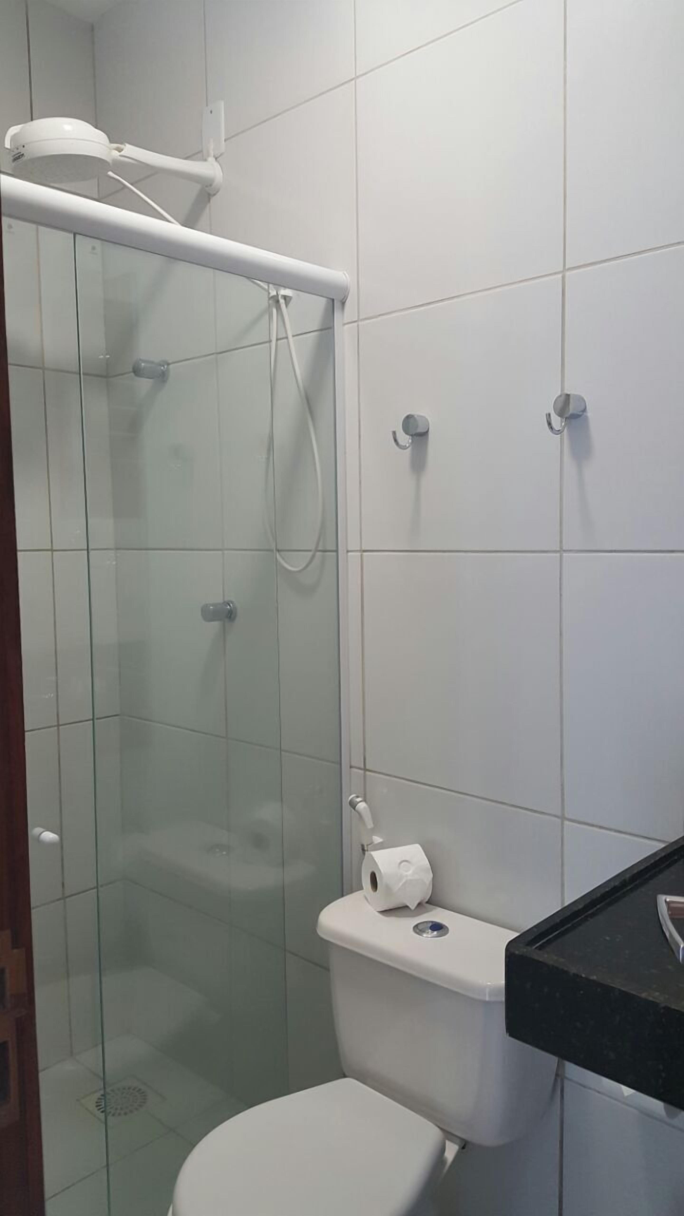 Een badkamer met een douche met glazen wand, een wit toilet en een zwart wastafelmeubel.