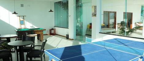 Una habitación con mesa de ping pong, sillas, mesa de billar y mesa de futbolín.