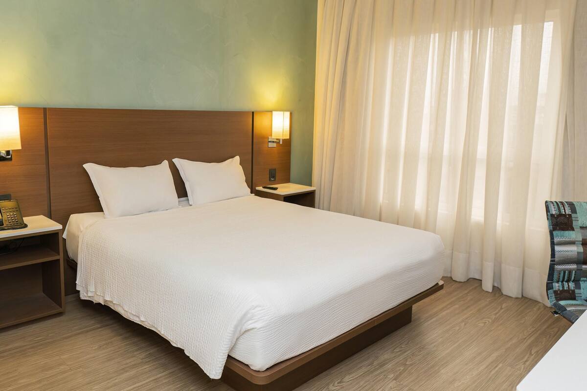 Une chambre d’hôtel avec un grand lit, des lampes de chevet, une table de chevet et une fenêtre avec des rideaux.