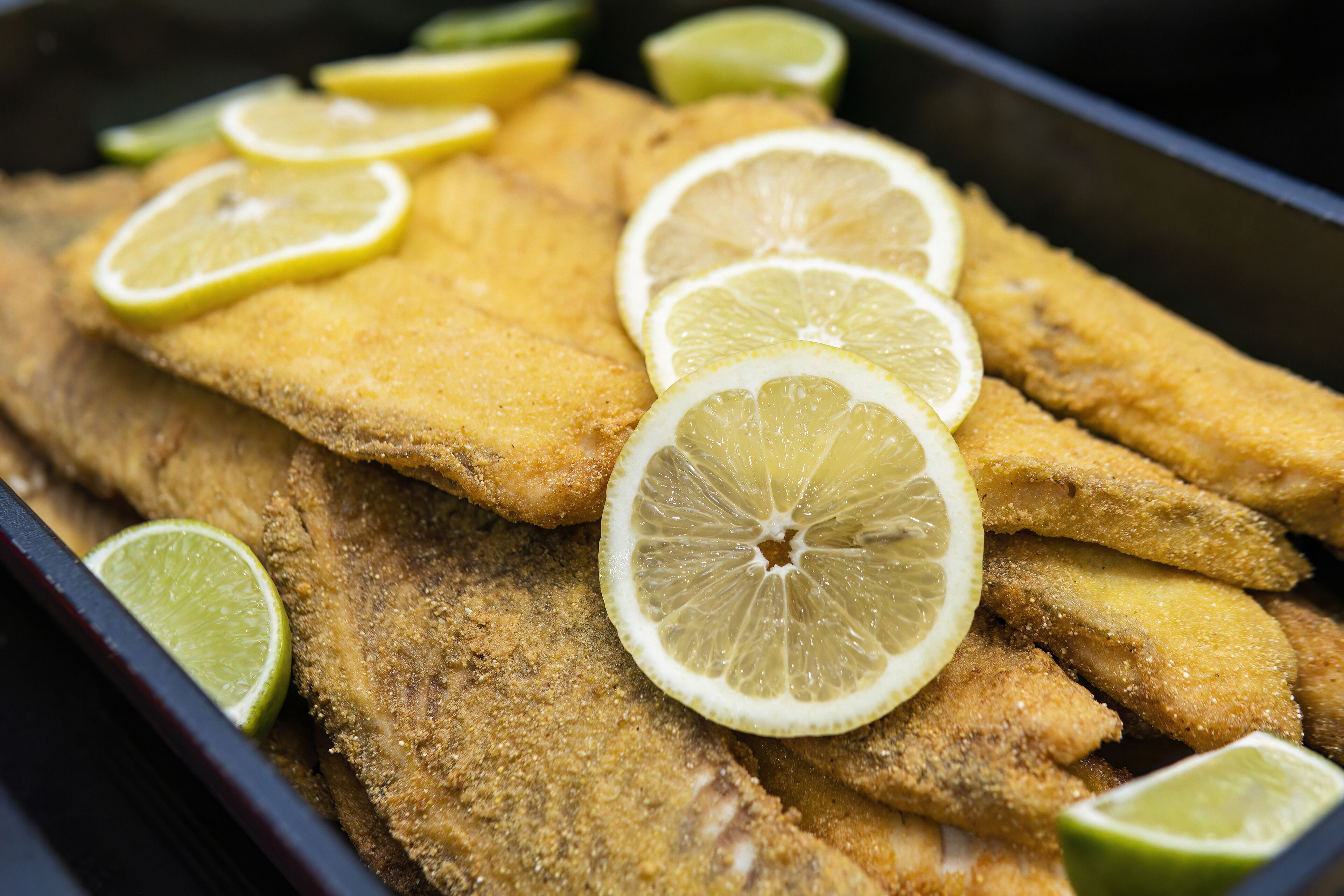Una bandeja de filetes de pescado empanizados, decorados con rodajas de limón.
