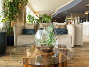 Un salon moderne avec une table basse en verre, un canapé beige et diverses plantes d’intérieur.