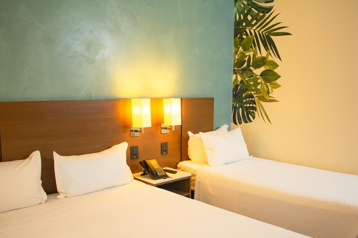 Une chambre d’hôtel avec deux lits, une table de chevet avec un téléphone et une télécommande, et des lampes fixées au mur.