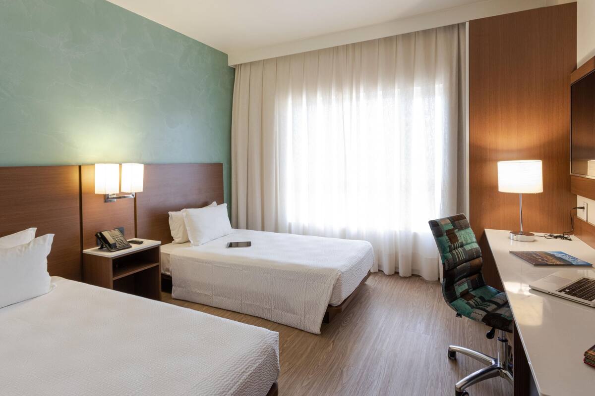 Une chambre d’hôtel avec deux lits, un bureau avec un ordinateur portable, une chaise, un téléphone et une lampe.