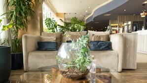 Un salon moderne avec une table basse en verre, un canapé beige et diverses plantes d’intérieur.
