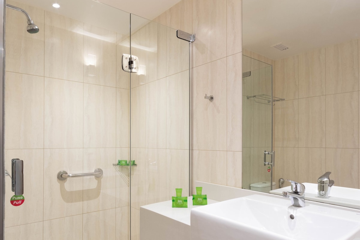 Een moderne badkamer met een douchecabine van glas, een grote spiegel en een witte wastafel.