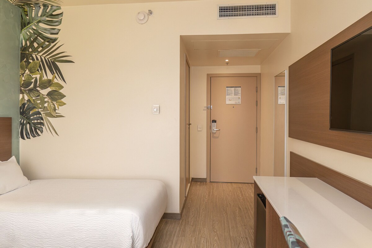 Een hotelkamer met een bed, een bureau, een spiegel en een deur naar een andere kamer.