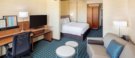 Ein Hotelzimmer mit Bett, Schreibtisch mit Fernseher, Sessel, Sofa, zwei kleinen Tischen und einem gemusterten Teppich.