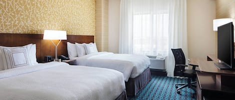 A hotel room with two beds, a desk, a chair, a television, and a patterned carpet.
